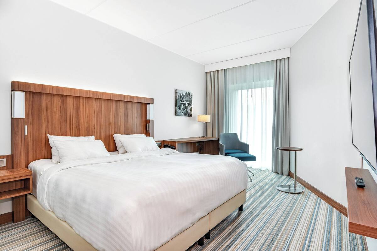 Hotellihuone, jossa on suuri sänky, työpöytä, tuoli, televisio ja ikkuna, jossa on verhot.