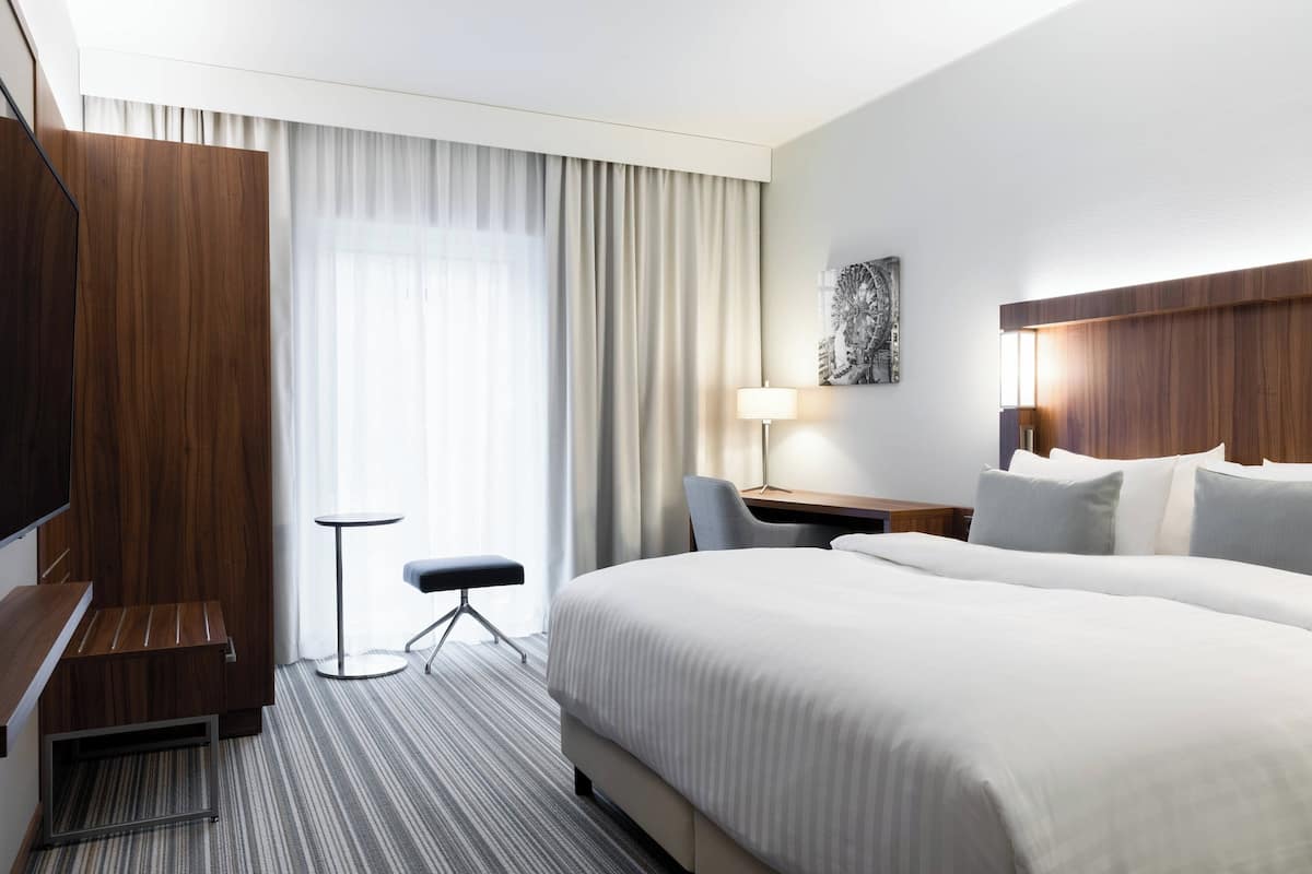 Hotellihuone, jossa on suuri sänky, työpöytä tuolilla, pieni pöytä ja televisio.