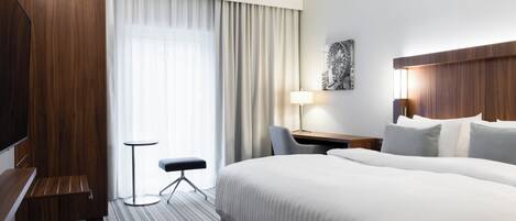 A hotel room with a large bed, a desk with a chair, a small table, and a TV.