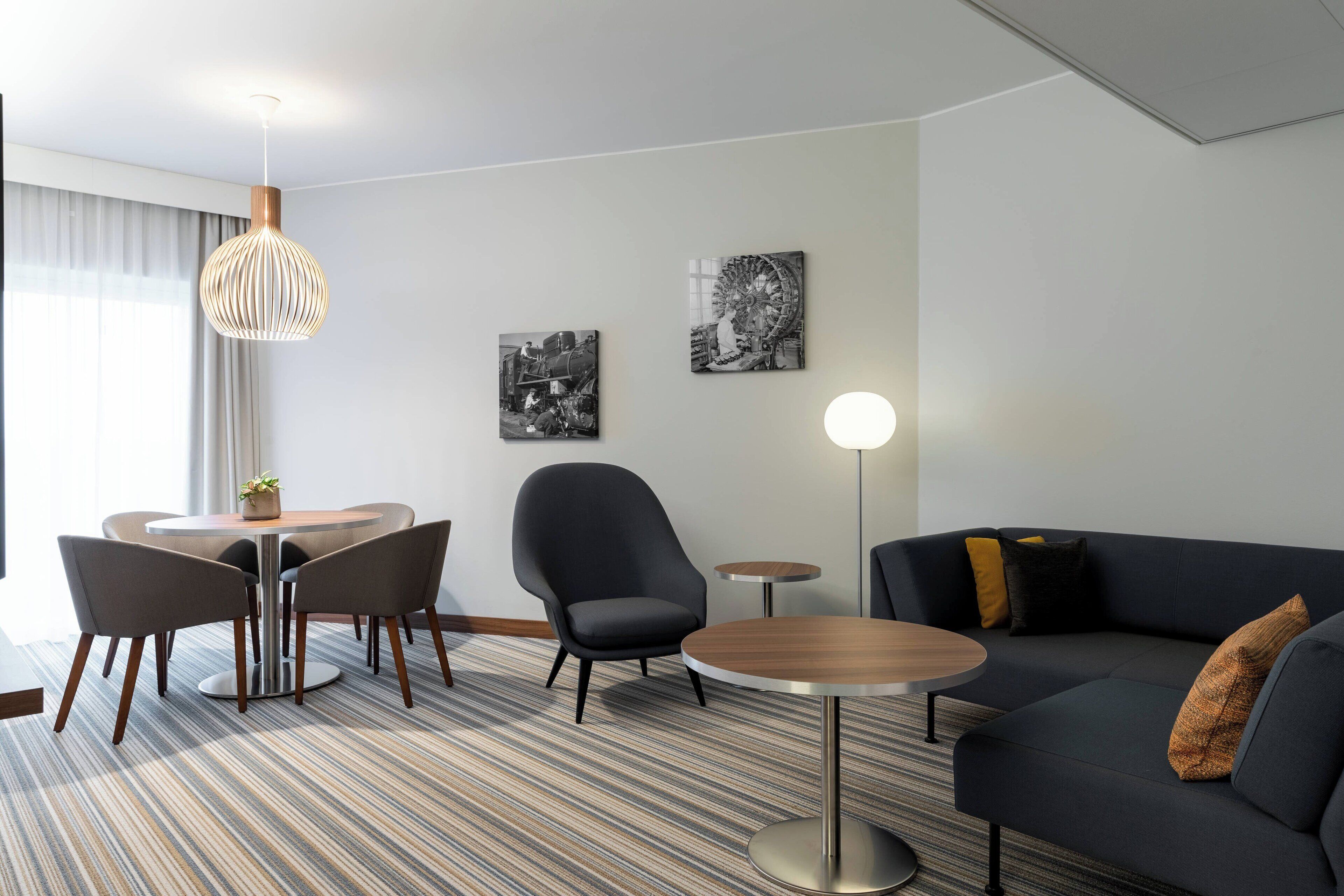 Una habitación de hotel moderna con comedor, sofá y dos obras de arte en la pared.