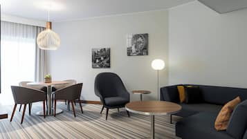 Una habitación de hotel moderna con comedor, sofá y dos obras de arte en la pared.