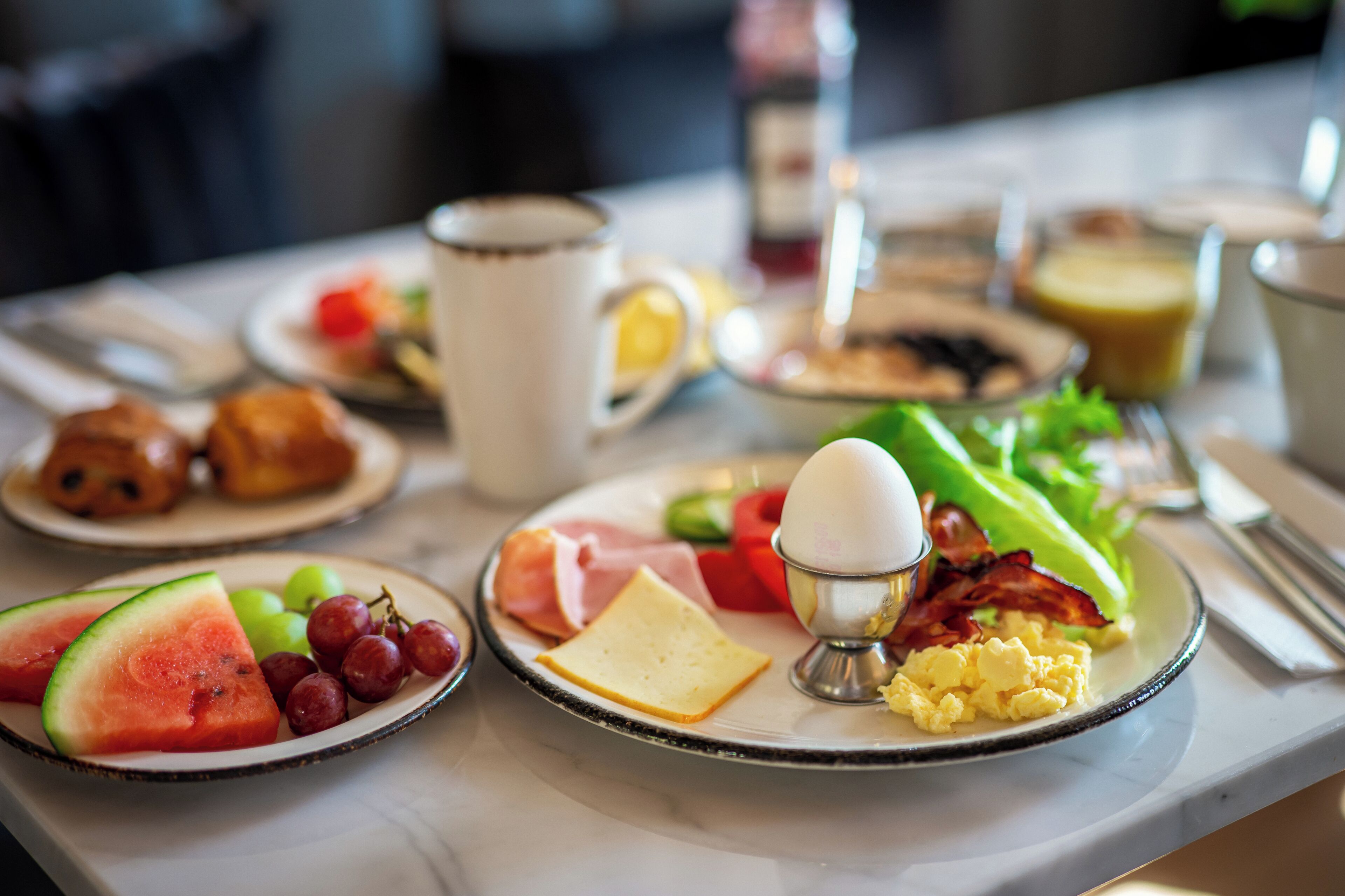 A breakfast table with plates of food, including eggs, bacon, cheese, and fruits.