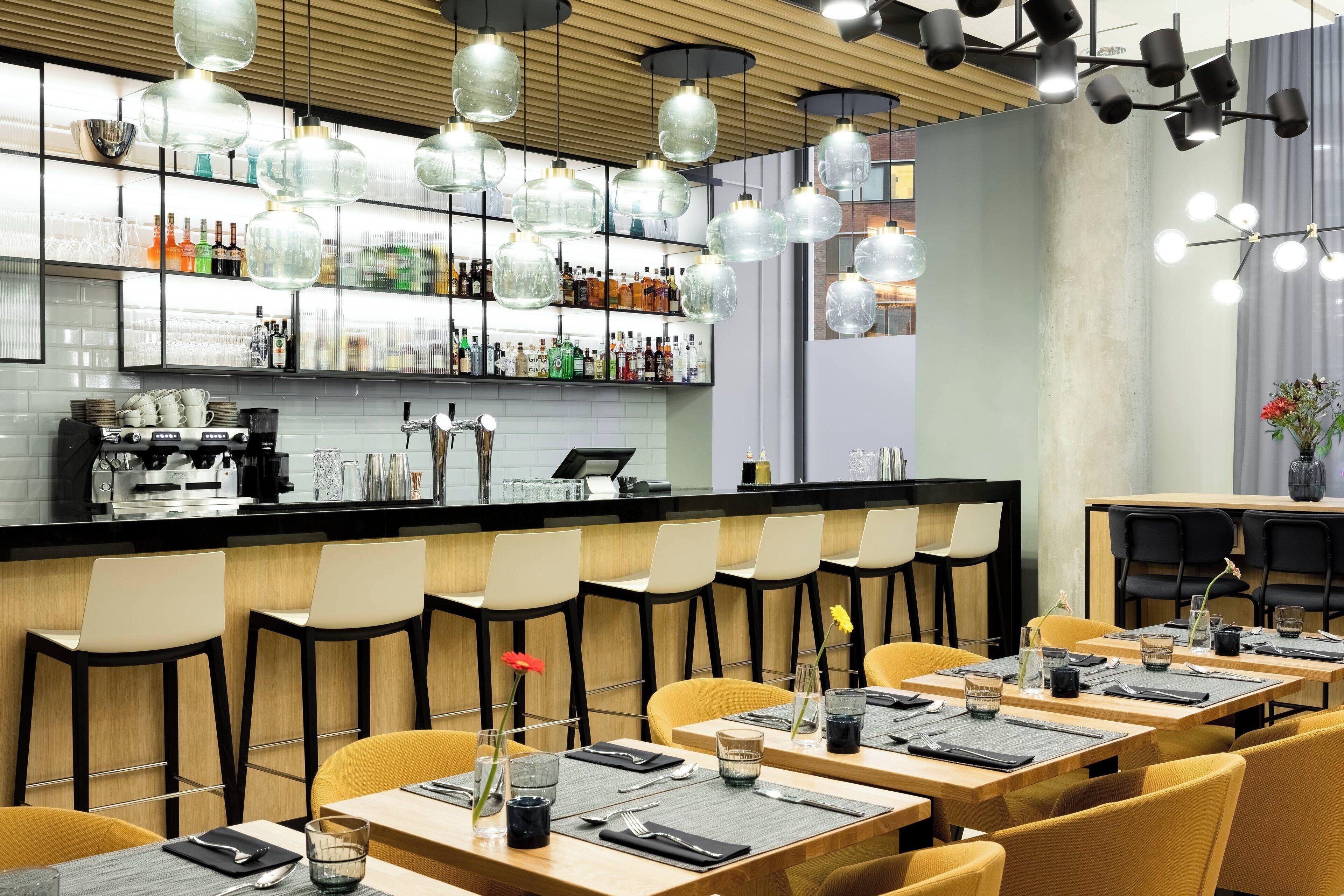 En modern restaurang med en bardel, flera olika typer av sittplatser och ett varierat utbud av bordsarrangemang.