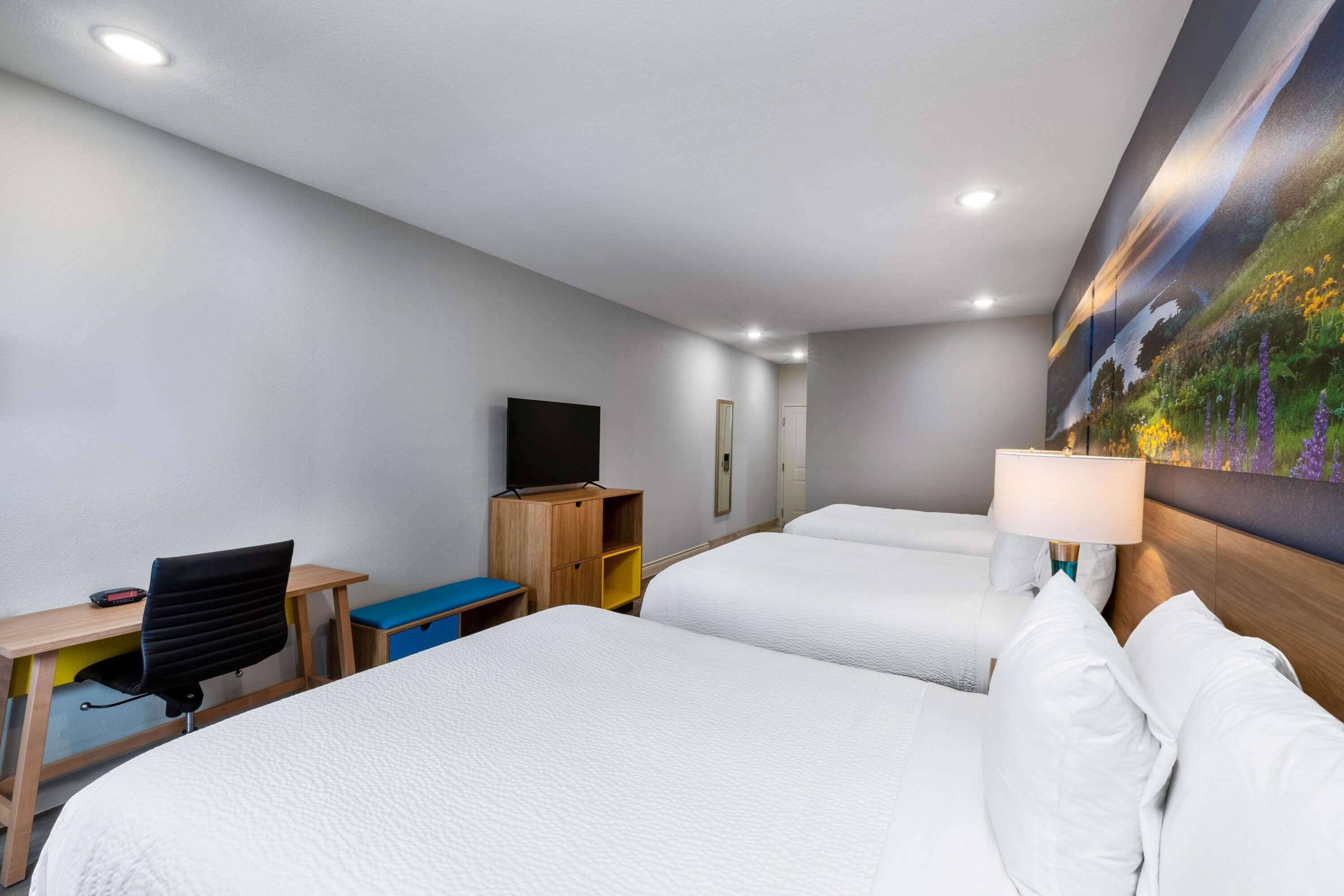 A hotel room with two beds, a desk, a chair, a TV, and a painting on the wall.