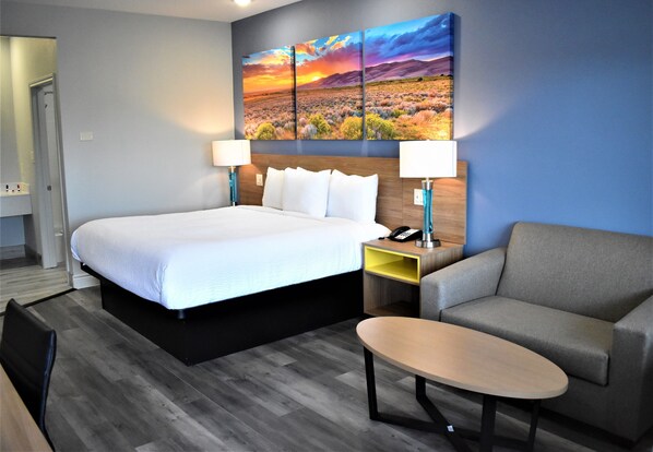 Quarto de hotel com uma cama grande, um sofá, uma mesinha e um quadro de uma paisagem de pôr do sol na parede.
