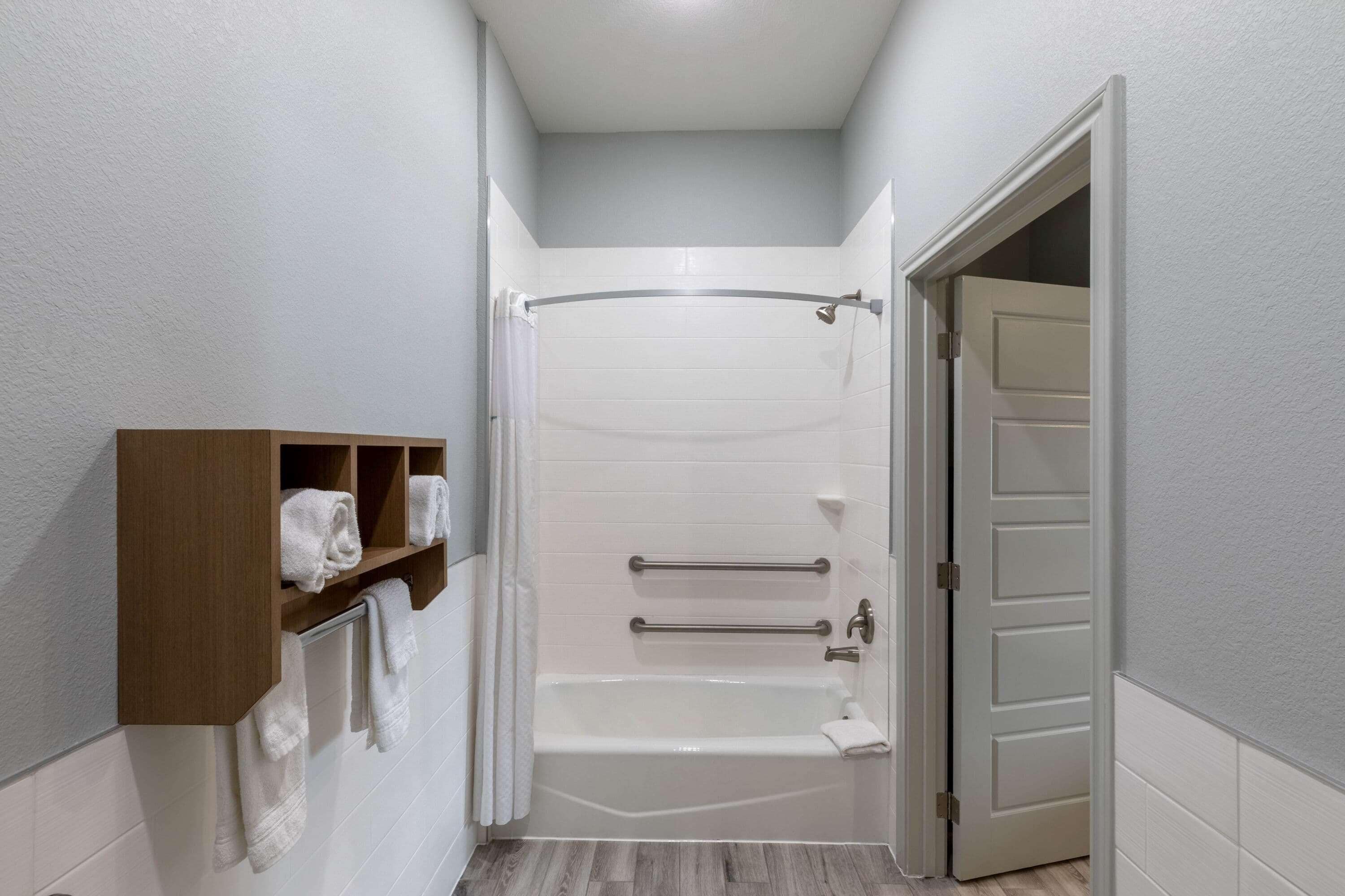 A bathroom with a bathtub, a shower curtain, a towel rack, and a wooden shelf with towels.