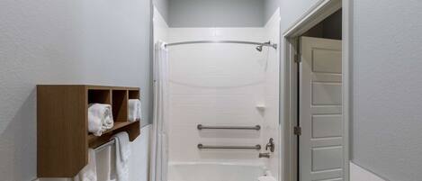 A bathroom with a bathtub, a shower curtain, a towel rack, and a wooden shelf with towels.