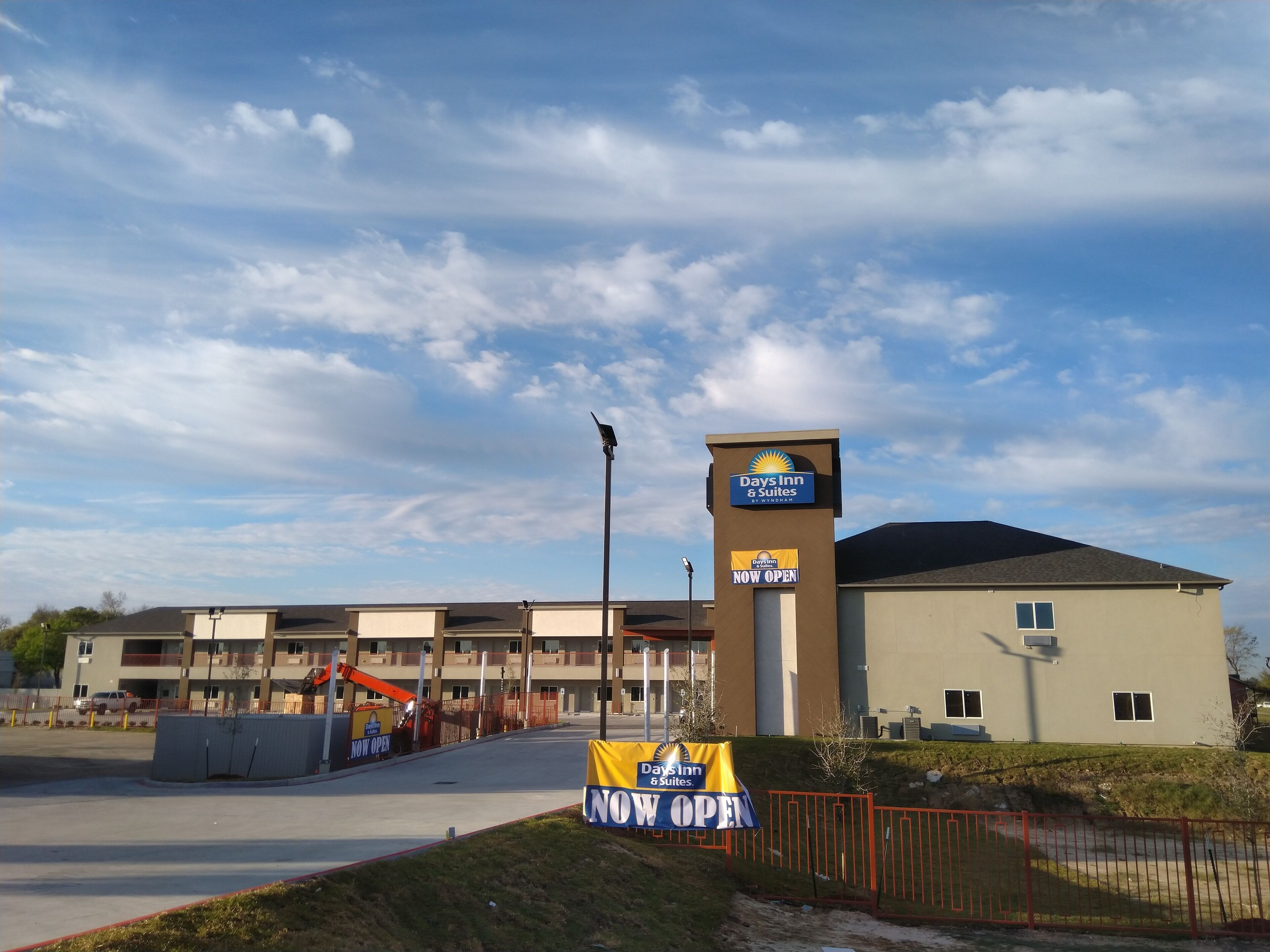 A Days Inn & Suites hotel with a 'NOW OPEN' sign, a parking lot, and a fenced construction area.