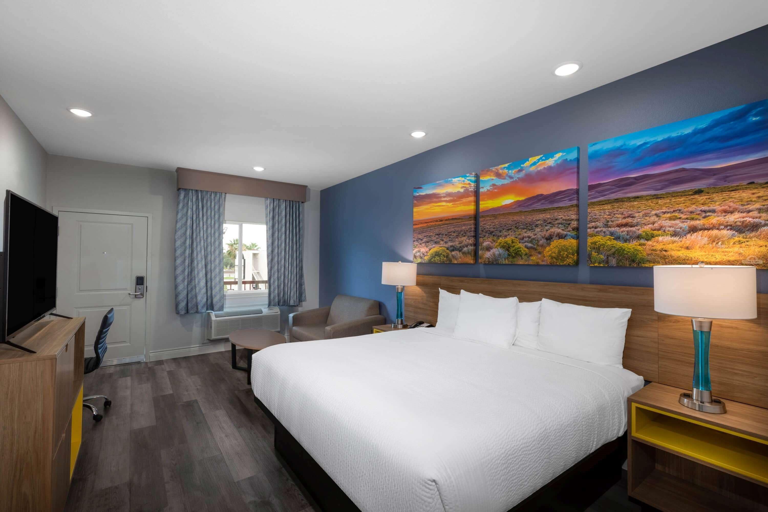 A hotel room with a large bed, a desk, a chair, a TV, and a painting on the wall.