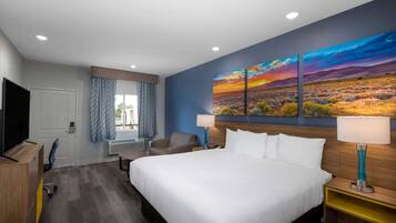 A hotel room with a large bed, a desk, a chair, a TV, and a painting on the wall.