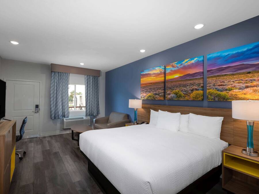 A hotel room with a large bed, a desk, a chair, a TV, and a painting on the wall.
