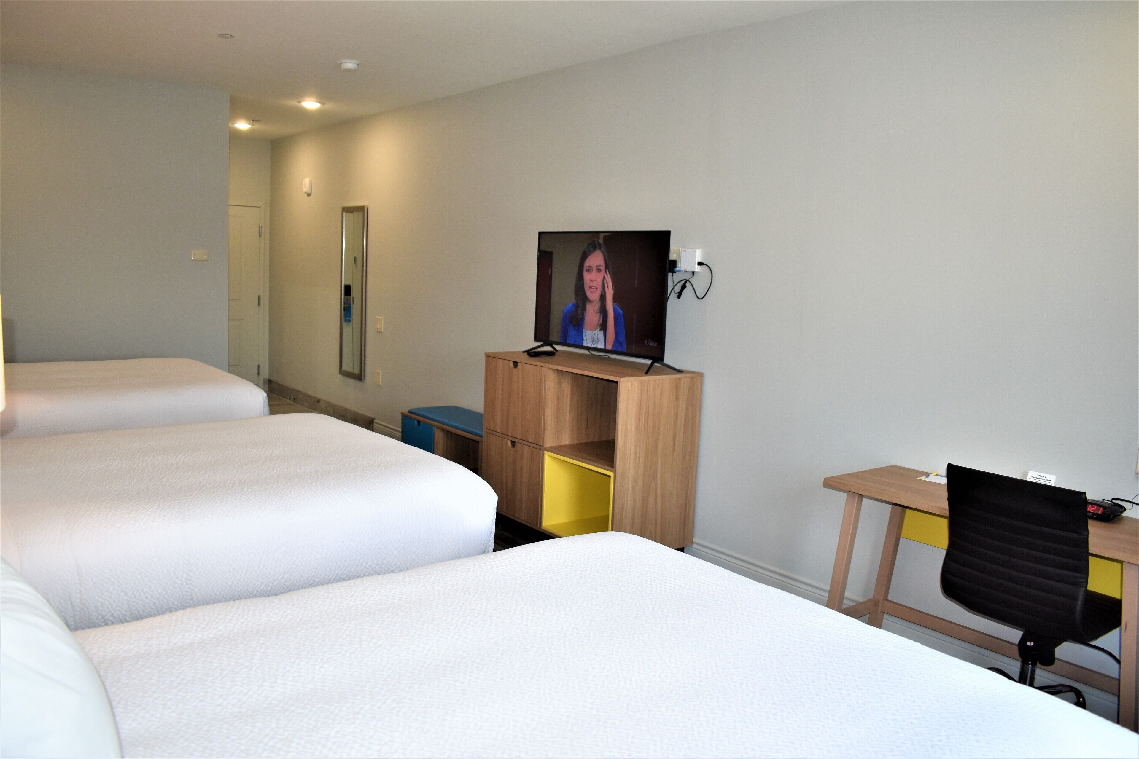 A hotel room with three beds, a desk with a chair, a television, and a mirror.