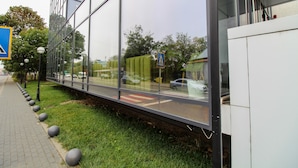 Um edifício moderno com grandes janelas de vidro que refletem a rua e carros estacionados.