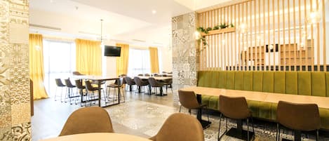 A modern dining area with a long wooden table, multiple chairs, and a green cushioned bench.