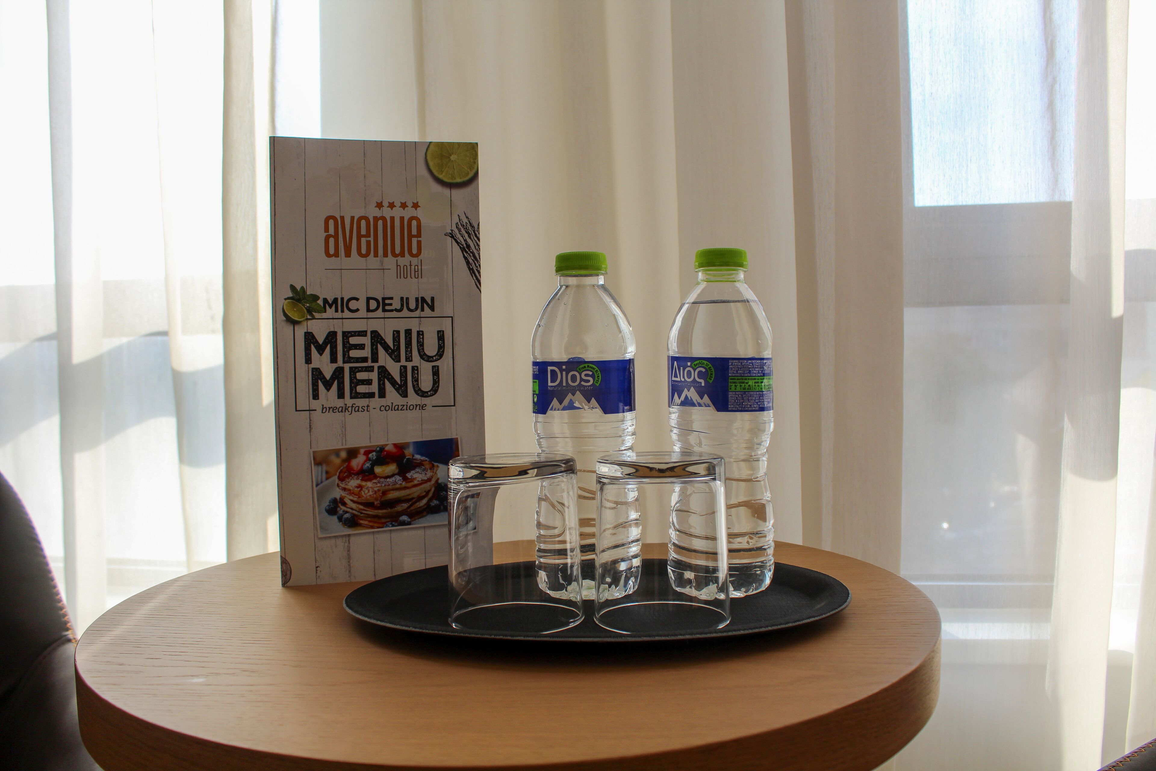 Una mesa de desayuno con un menú, dos botellas de agua y tres vasos.