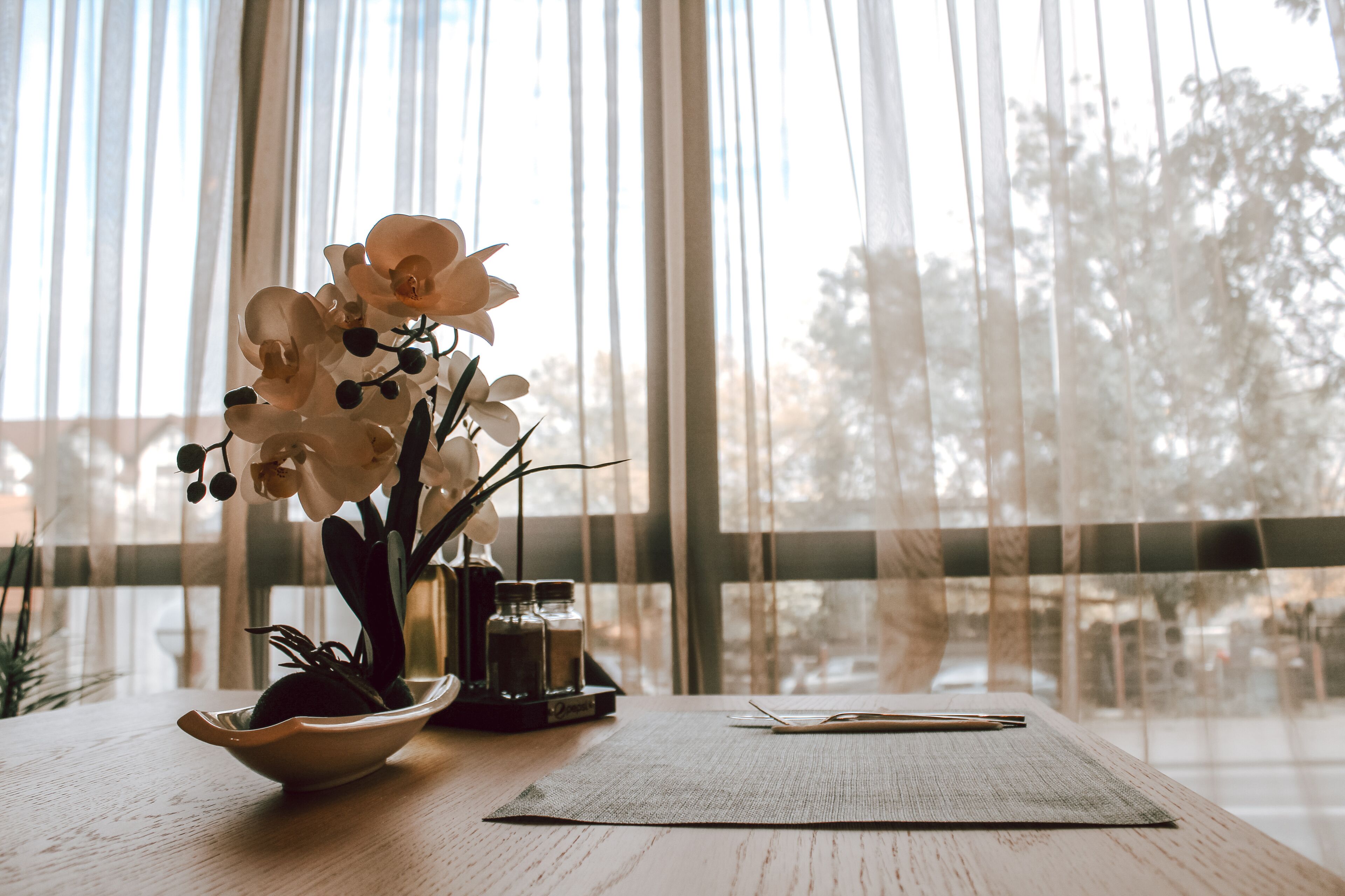 A wooden table with a vase of white orchids, a small bowl, and a pair of chopsticks.