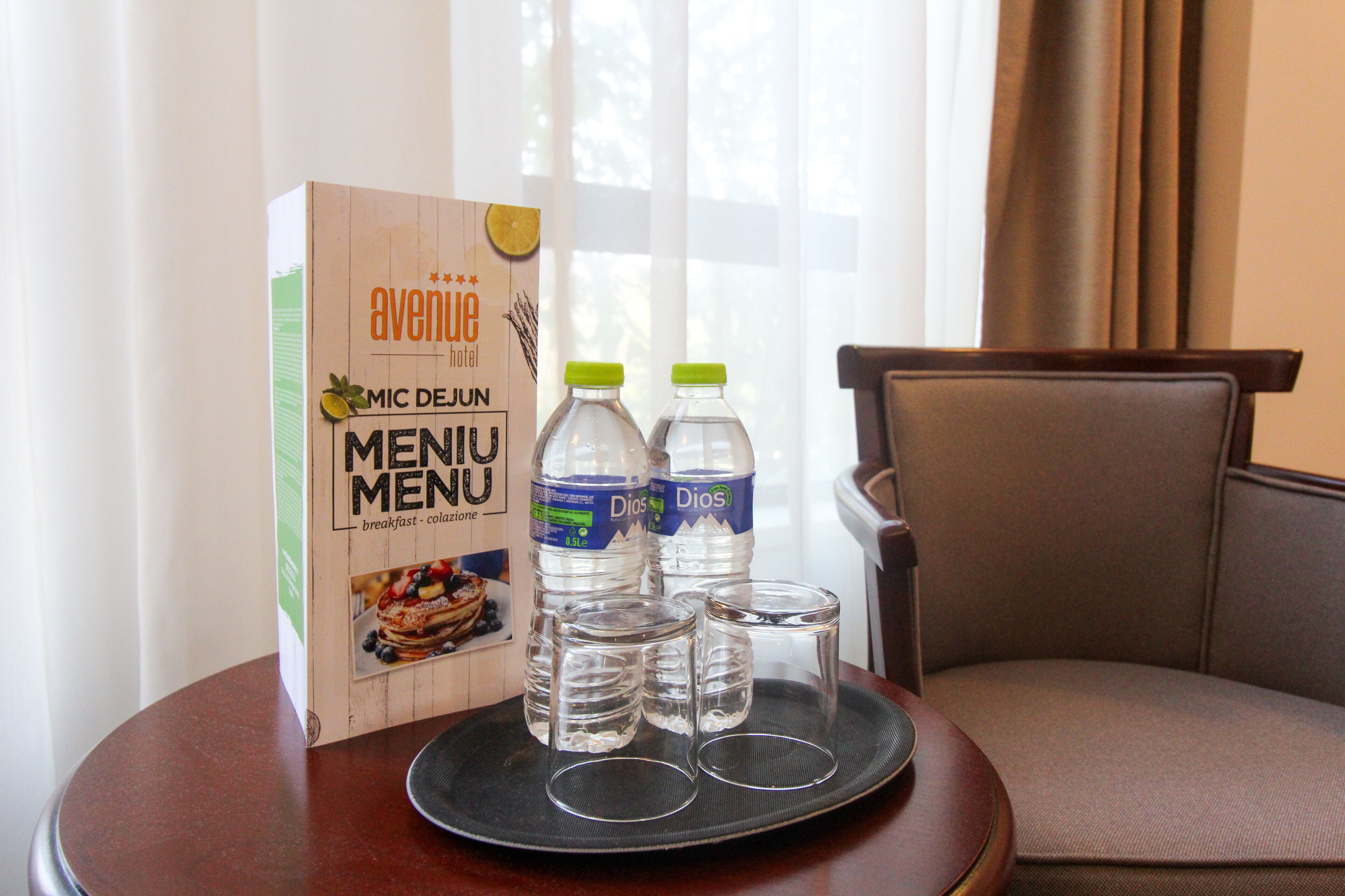 A hotel room with a breakfast menu box, two water bottles, and three glasses on a tray.