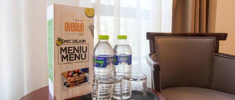 A hotel room with a breakfast menu box, two water bottles, and three glasses on a tray.