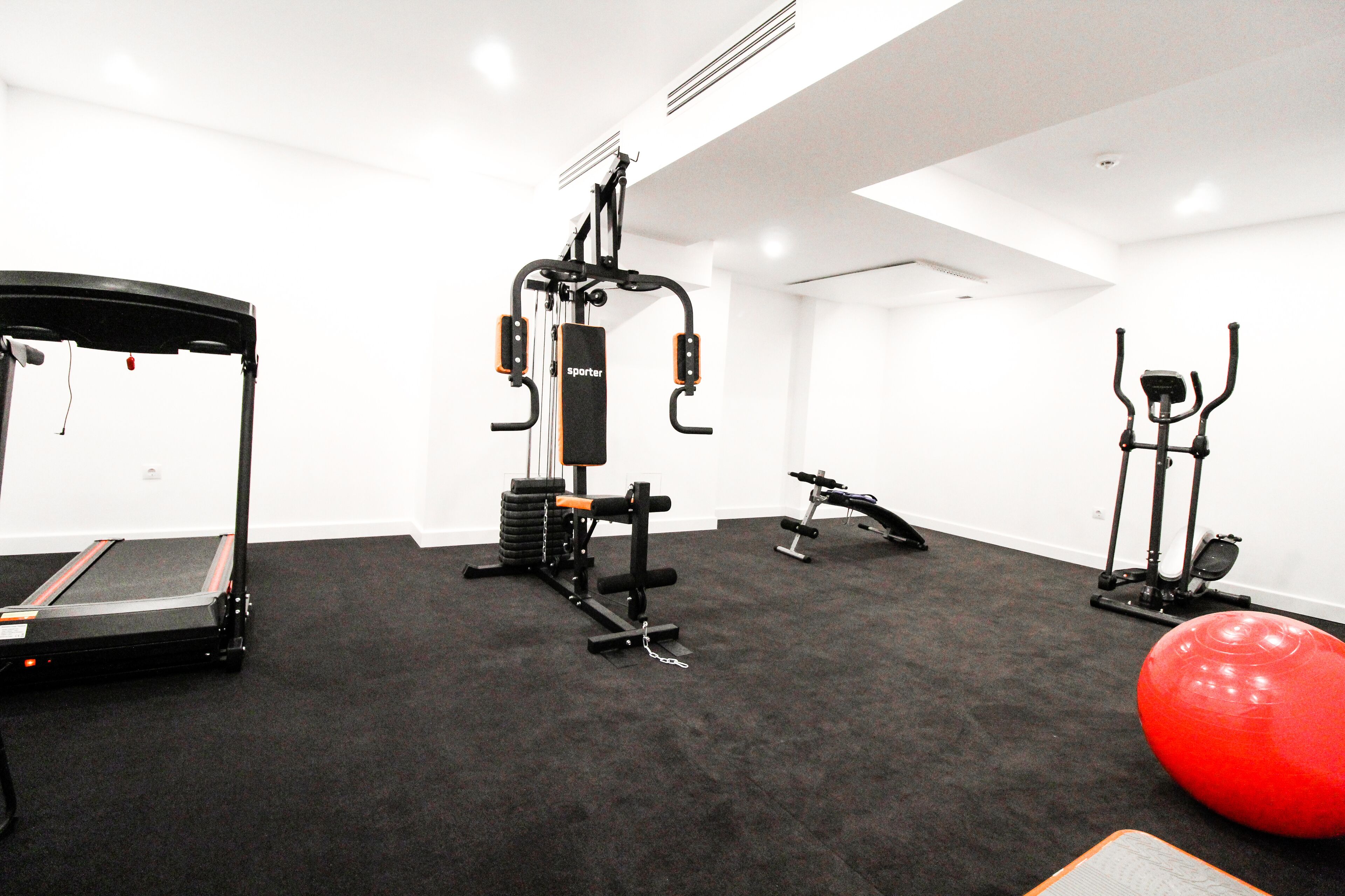 A gym with a treadmill, weight machine, exercise ball, and stationary bike.