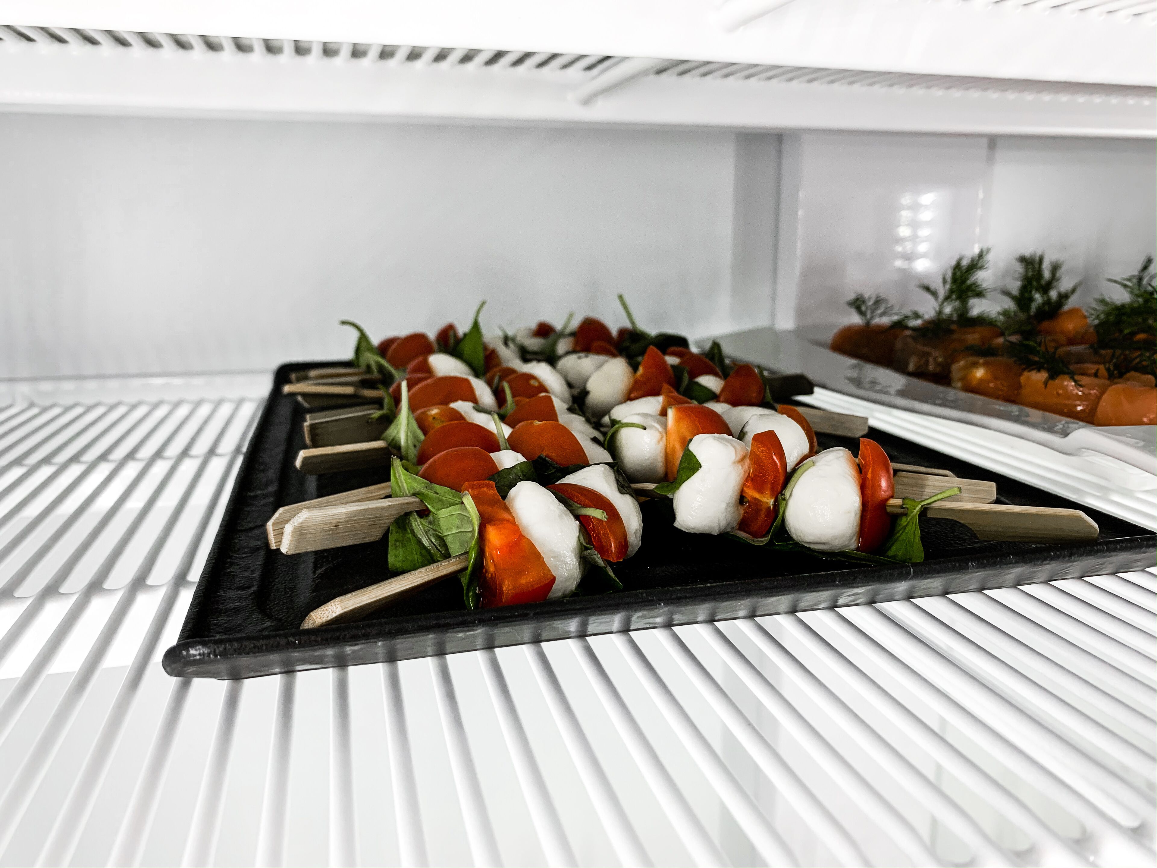 A refrigerator shelf with mozzarella and tomato skewers.