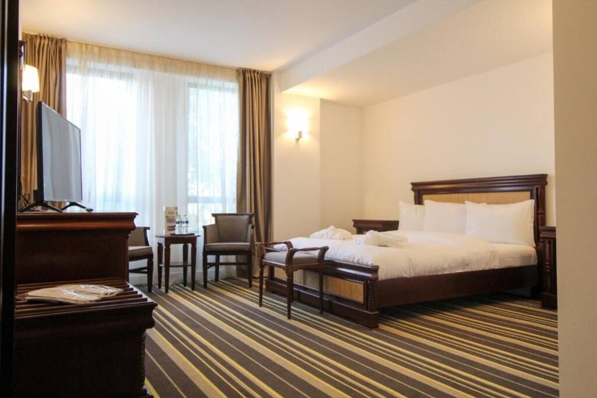 Ein Hotelzimmer mit einem Bett, einem Schreibtisch, einem Stuhl, einem Fernseher und einem Fenster mit Vorhängen.