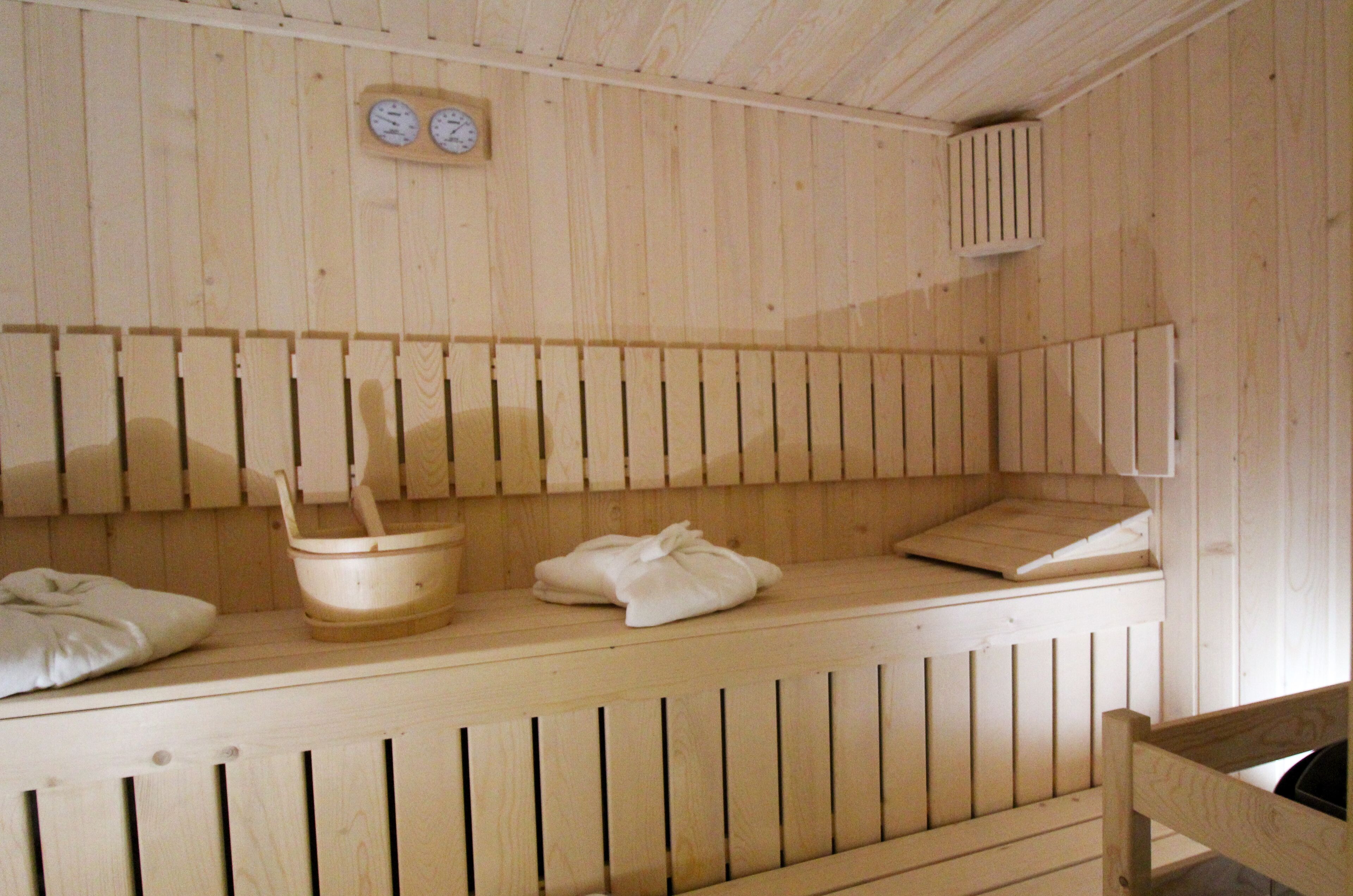 A wooden sauna with benches, a wooden bucket, and towels.