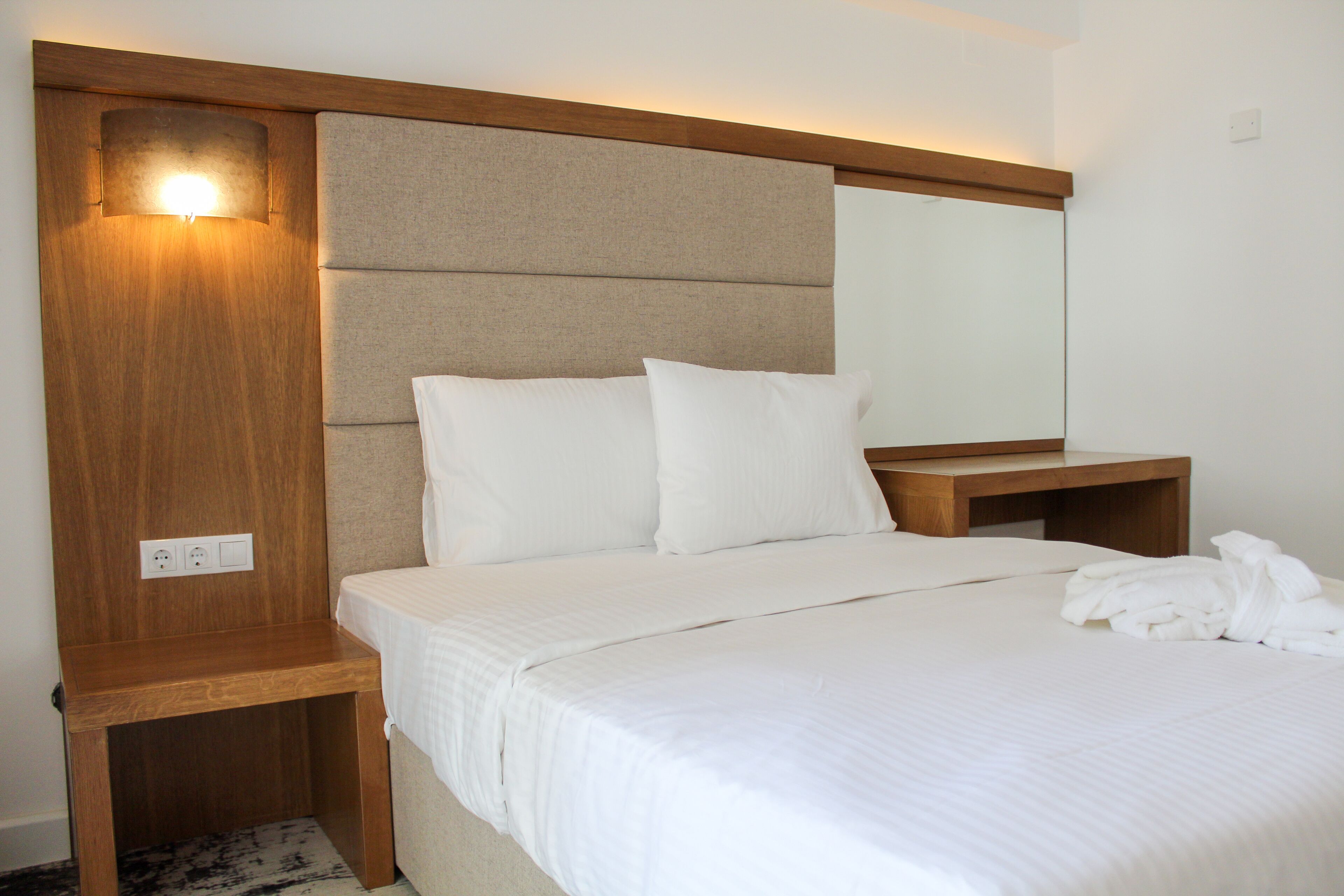 A hotel room with a wooden headboard, a large mirror, and a neatly made bed with white linens.