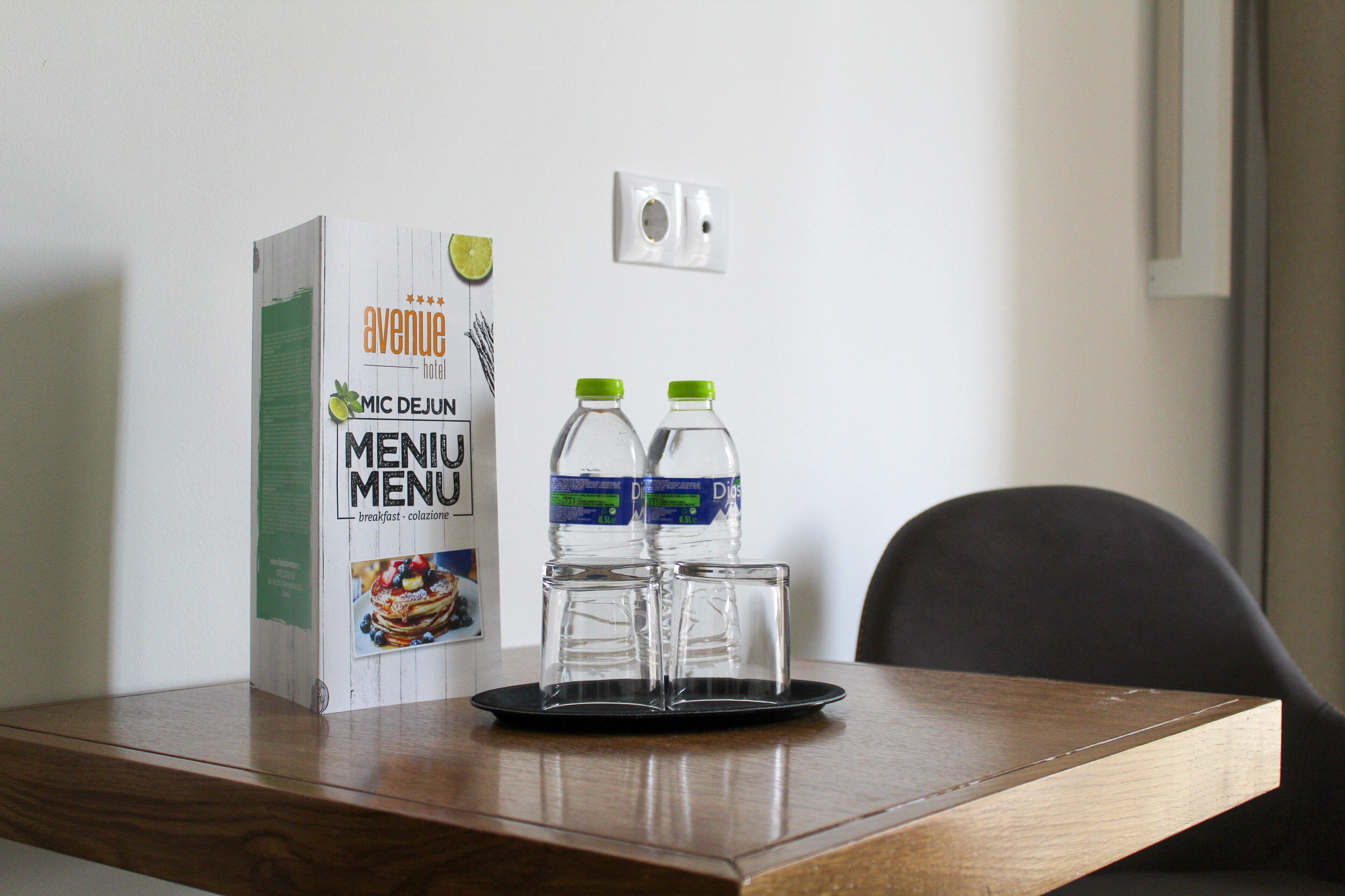 A breakfast menu box, two water bottles, and two glasses on a tray on a wooden table.