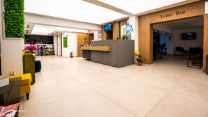 Um hall de entrada com balcão de recepção, bar no hall e uma tela de televisão.