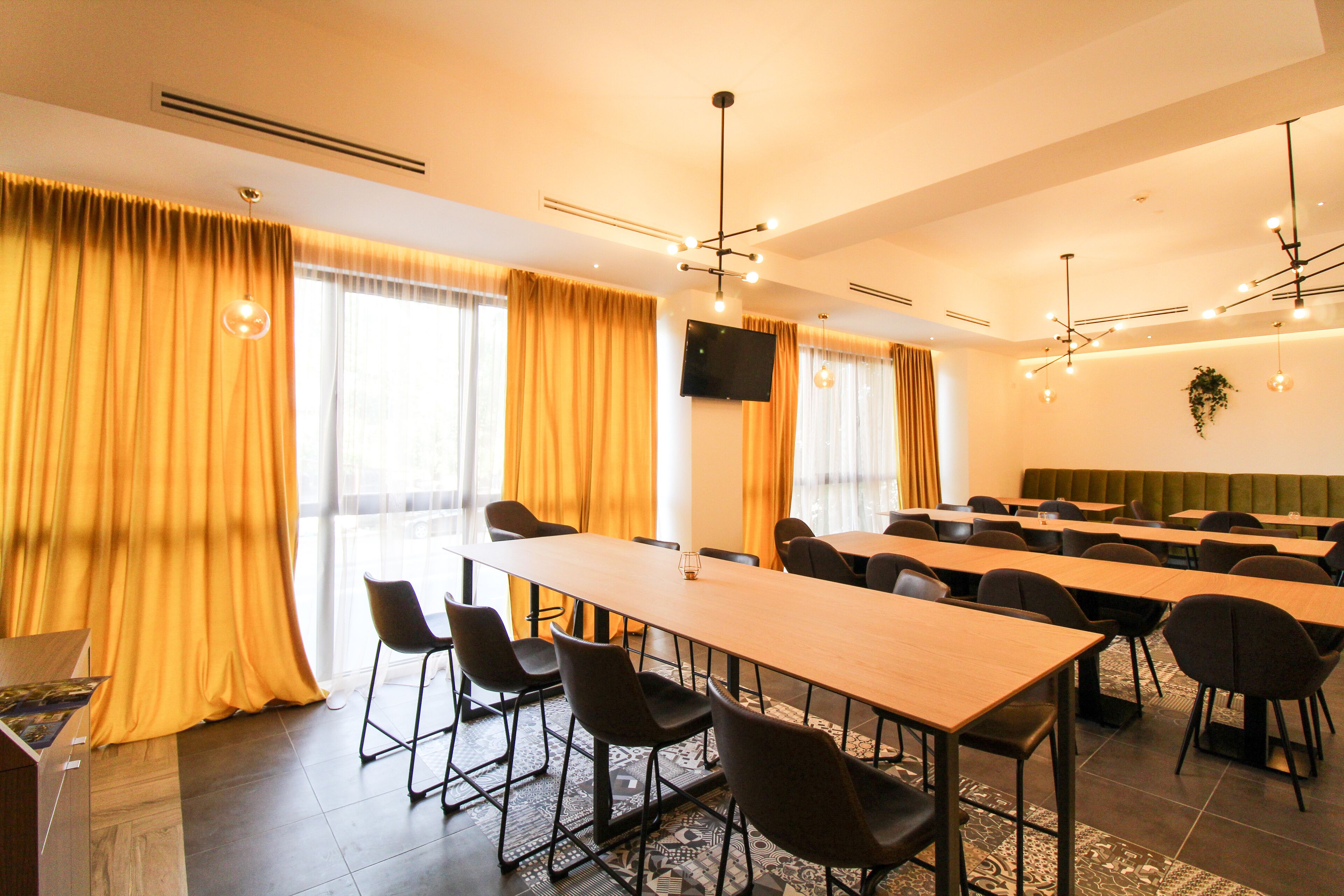 A conference room with long tables and chairs, a flat-screen TV, and large windows with curtains.