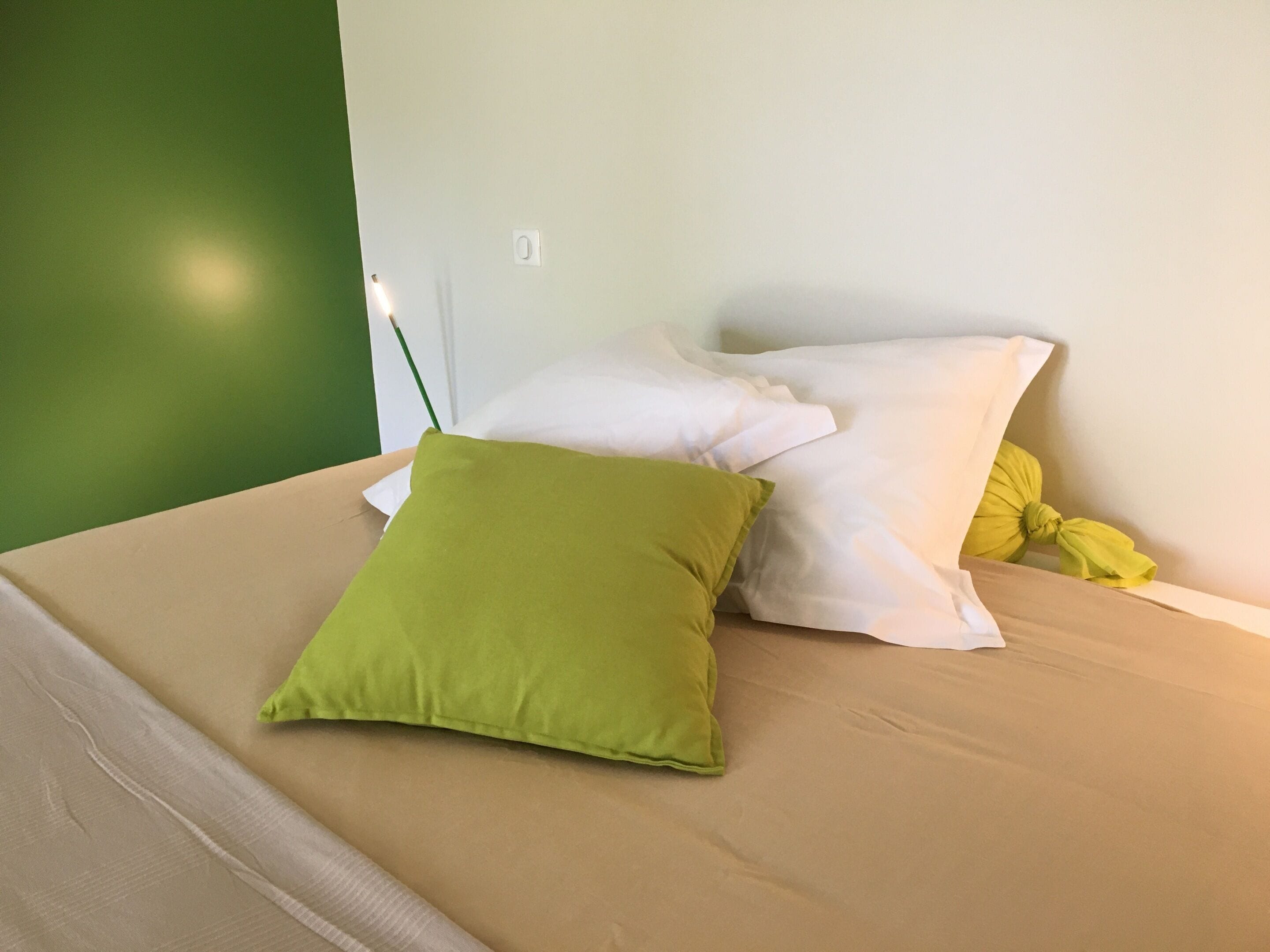 Een bed met beige beddengoed en twee kussens, een groen en een geel.