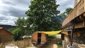 A rustic wooden cabin with a wooden deck, a hammock, and a wooden chair. - Le Jardin des 4M (Saint-Régis-du-Coin)