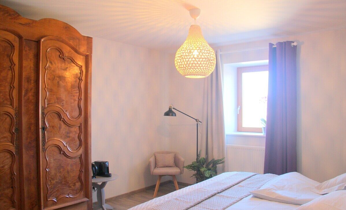 Un dormitorio con una cama, un armario de madera, un escritorio con lámpara y una ventana con cortinas.
