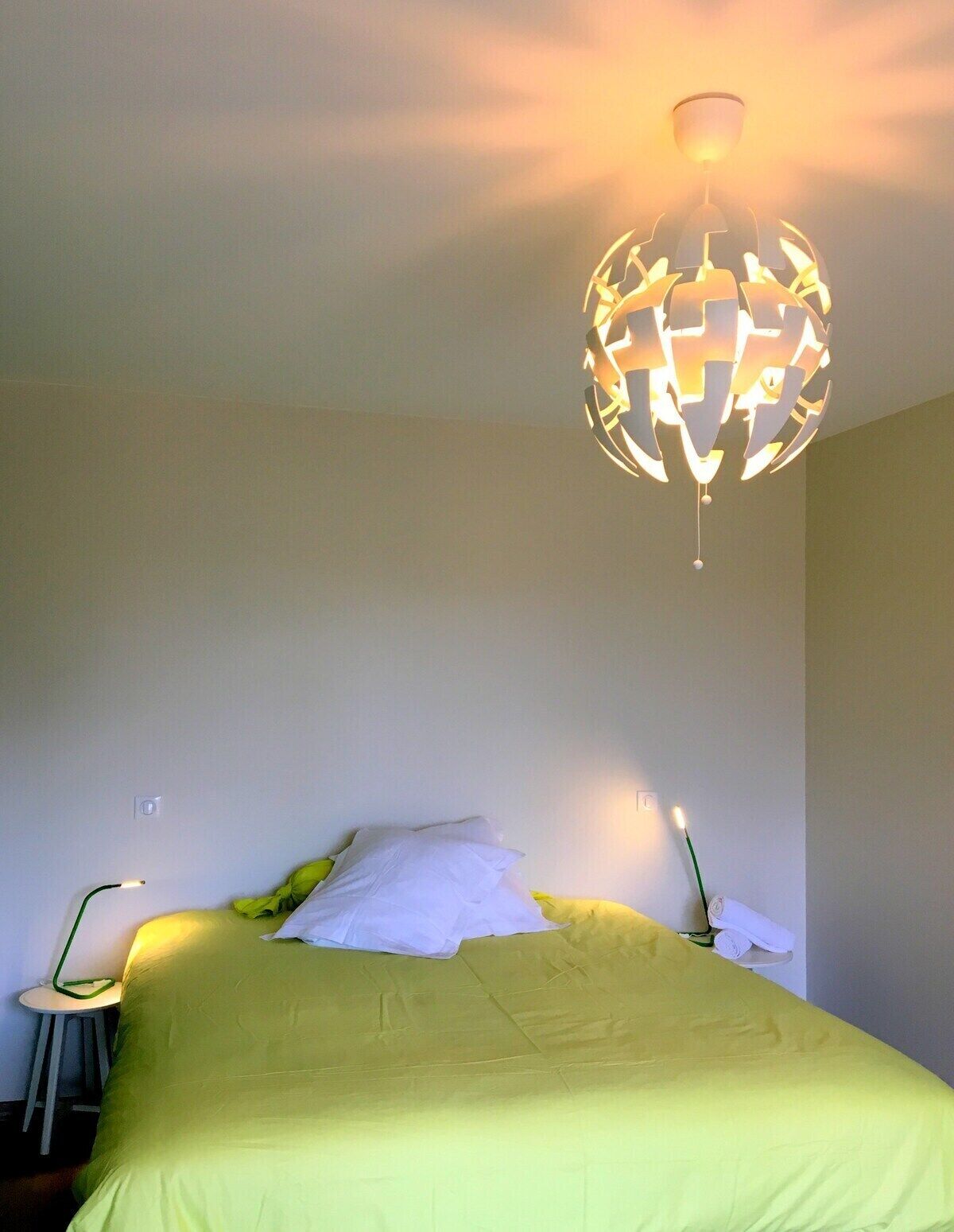 A bedroom with a bed, a bedside table, a lamp, and a unique spherical hanging light fixture.