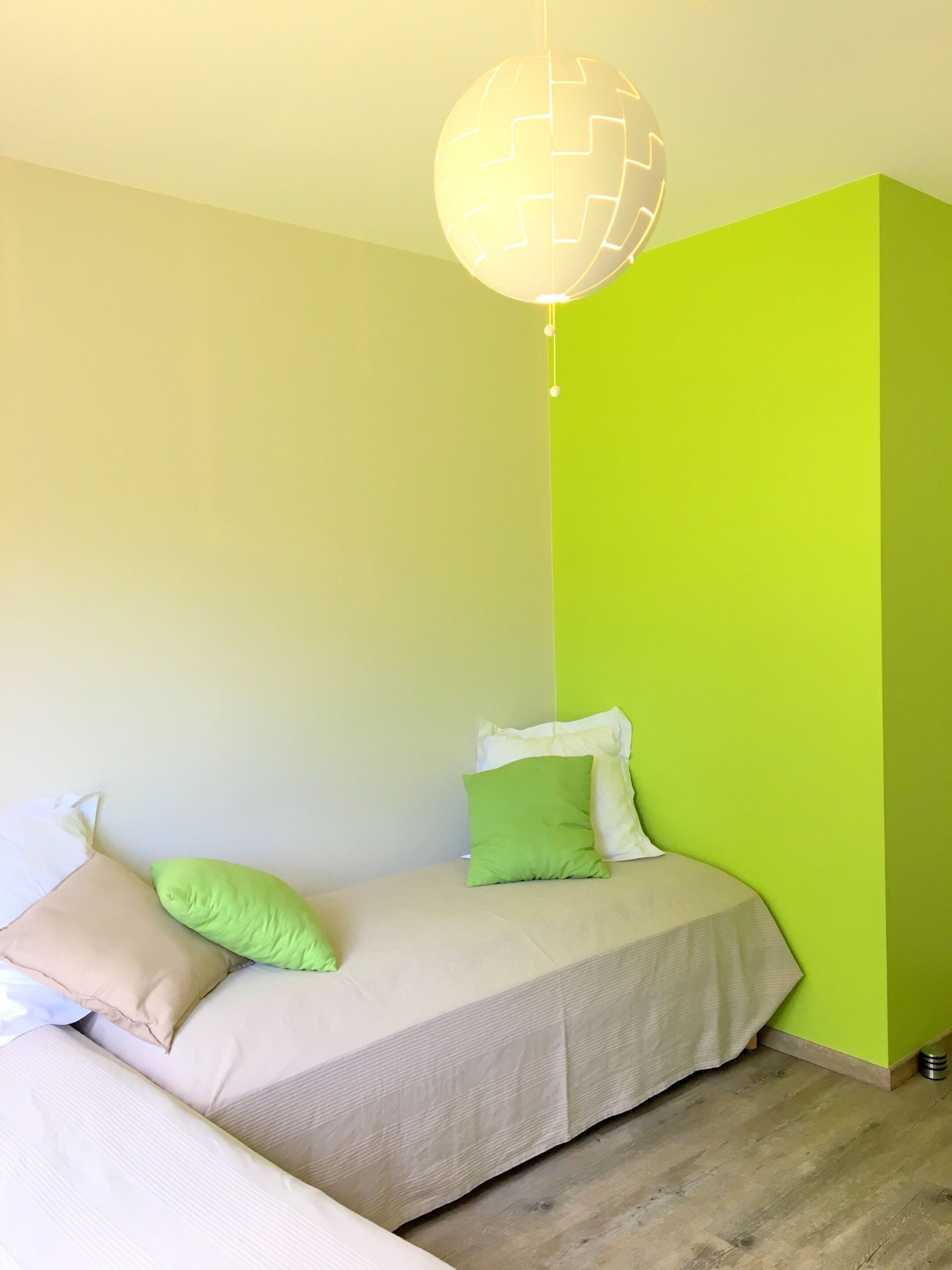 A small, neatly arranged bedroom with a bed, pillows, and a hanging light fixture.