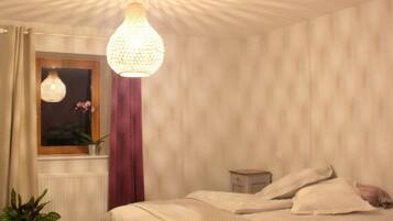 Een slaapkamer met een bed, een raam met gordijnen, een hanglamp en een nachtkastje.