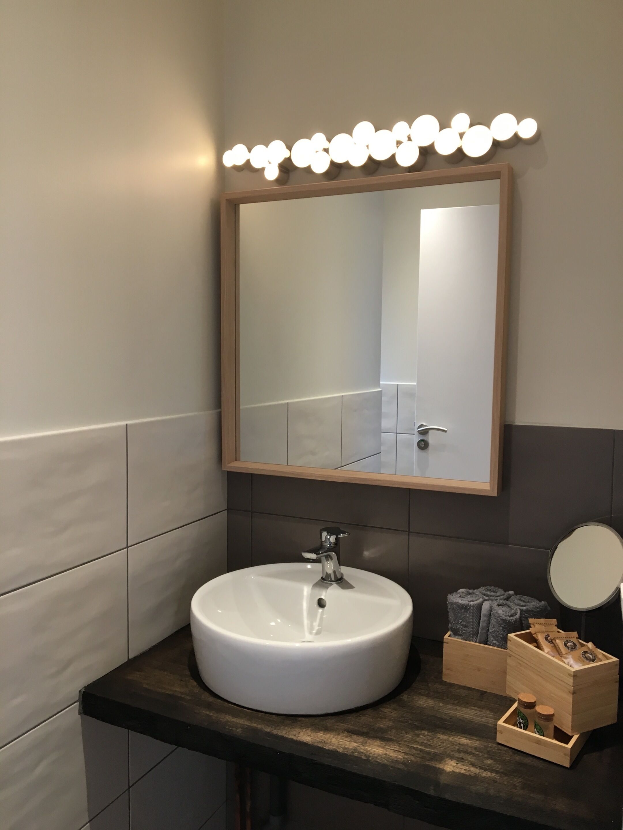 Un bagno con lavandino bianco, uno specchio e un mobile contenitore con un vassoio di legno porta articoli da toilette.