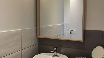 Un bagno con lavandino bianco, uno specchio e un mobile contenitore con un vassoio di legno porta articoli da toilette.