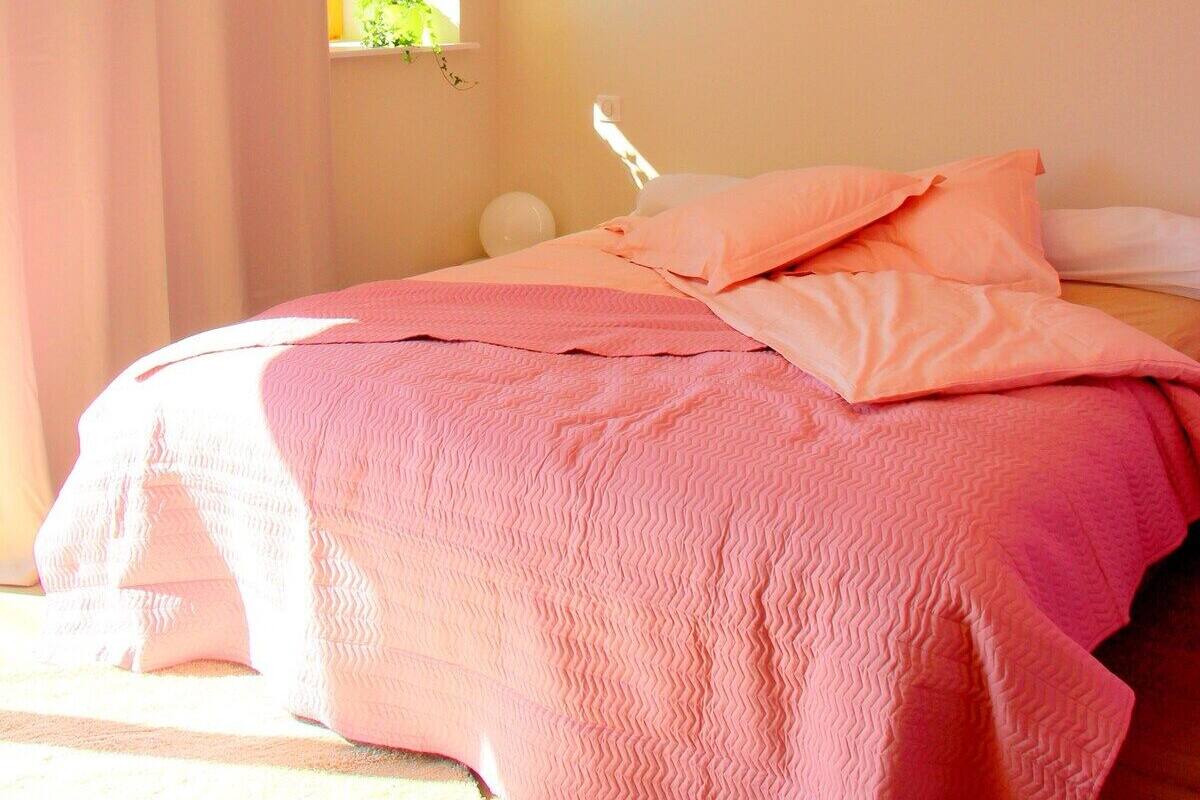 Een slaapkamer met een bed, een bedlampje en een raam met gordijnen.
