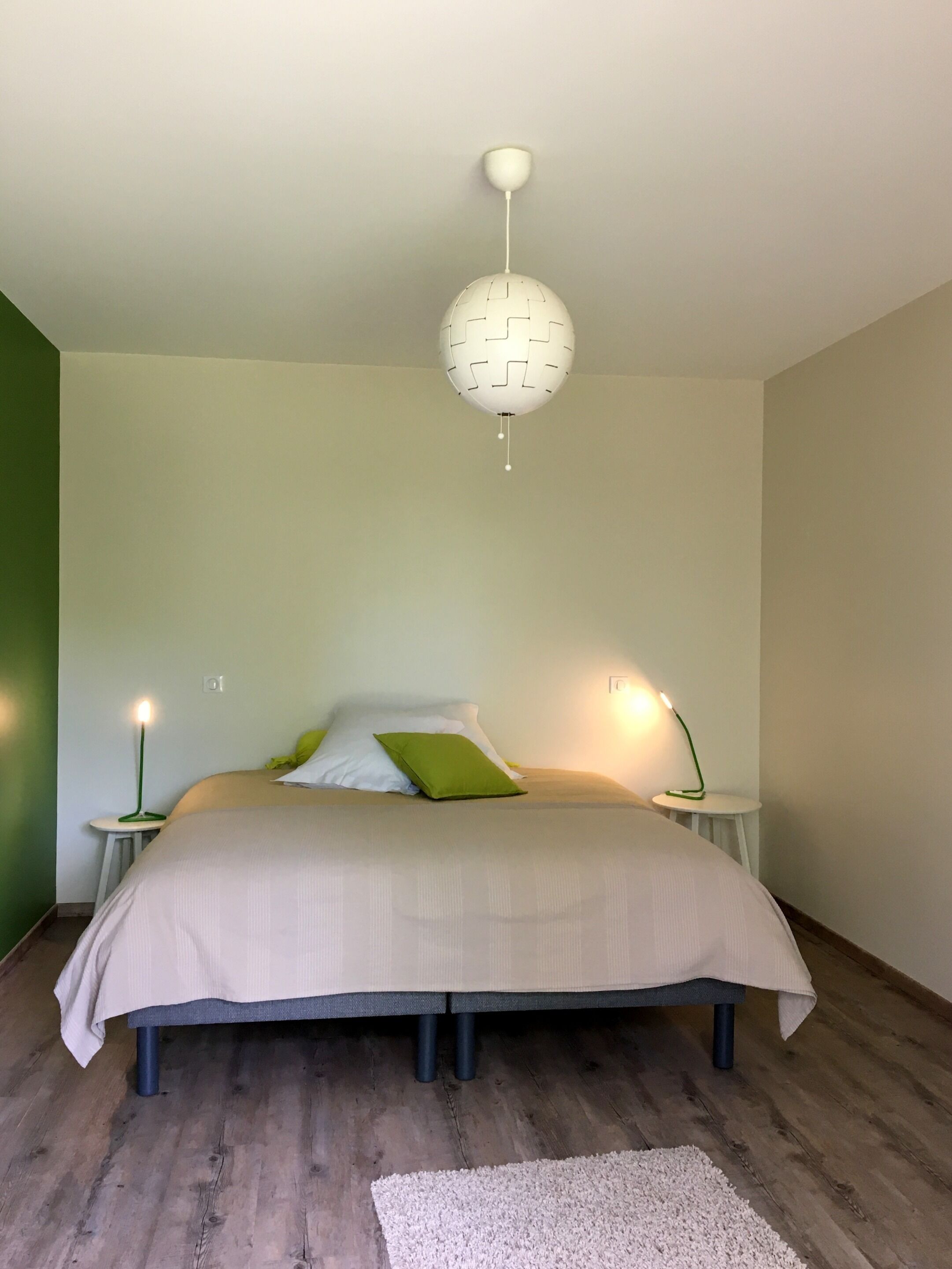 Une chambre à coucher avec un lit, des tables de chevet, un luminaire suspendu et un mur vert.