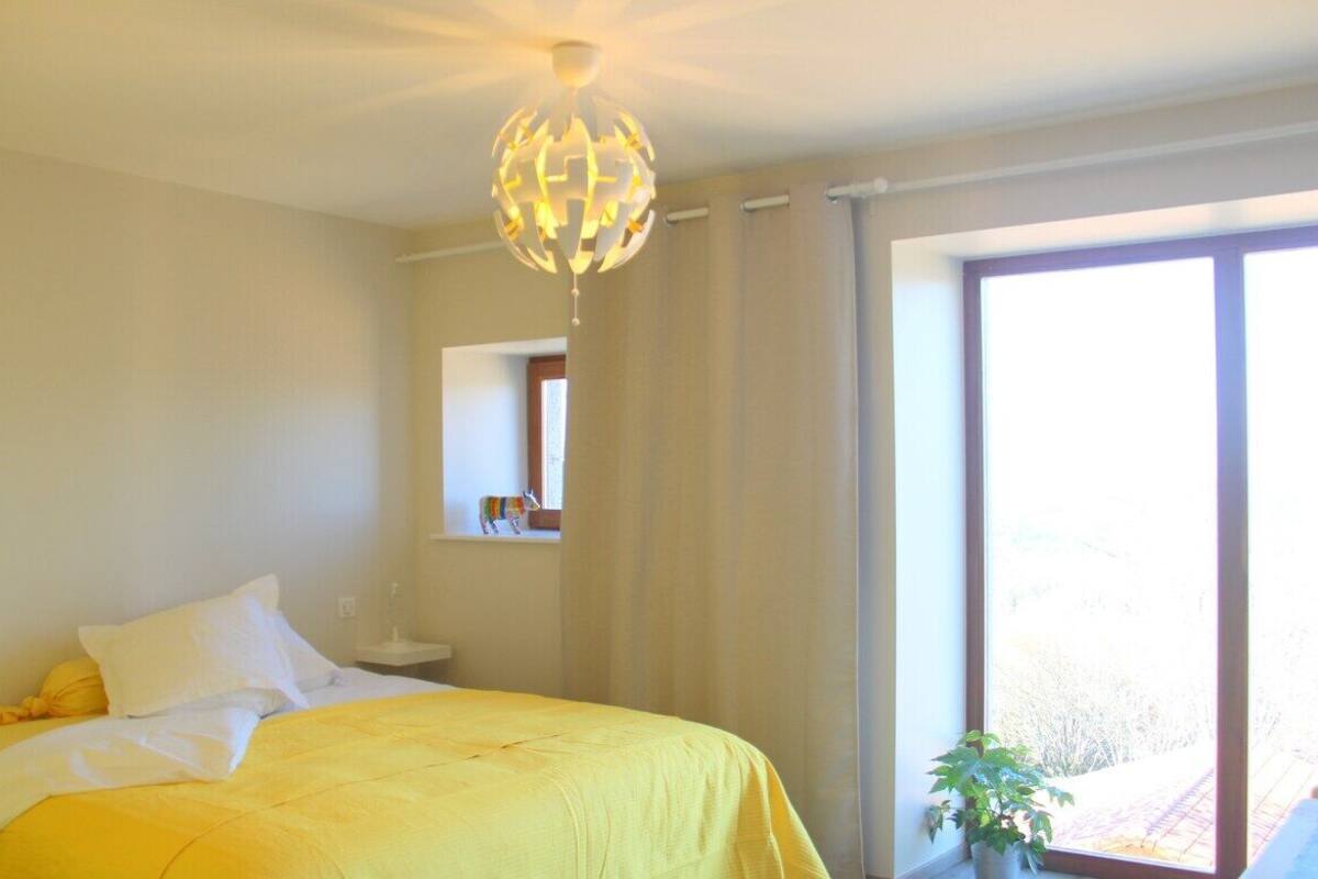 Een hotelkamer met een bed, een hanglamp, een raam met gordijnen en een kleine plant.