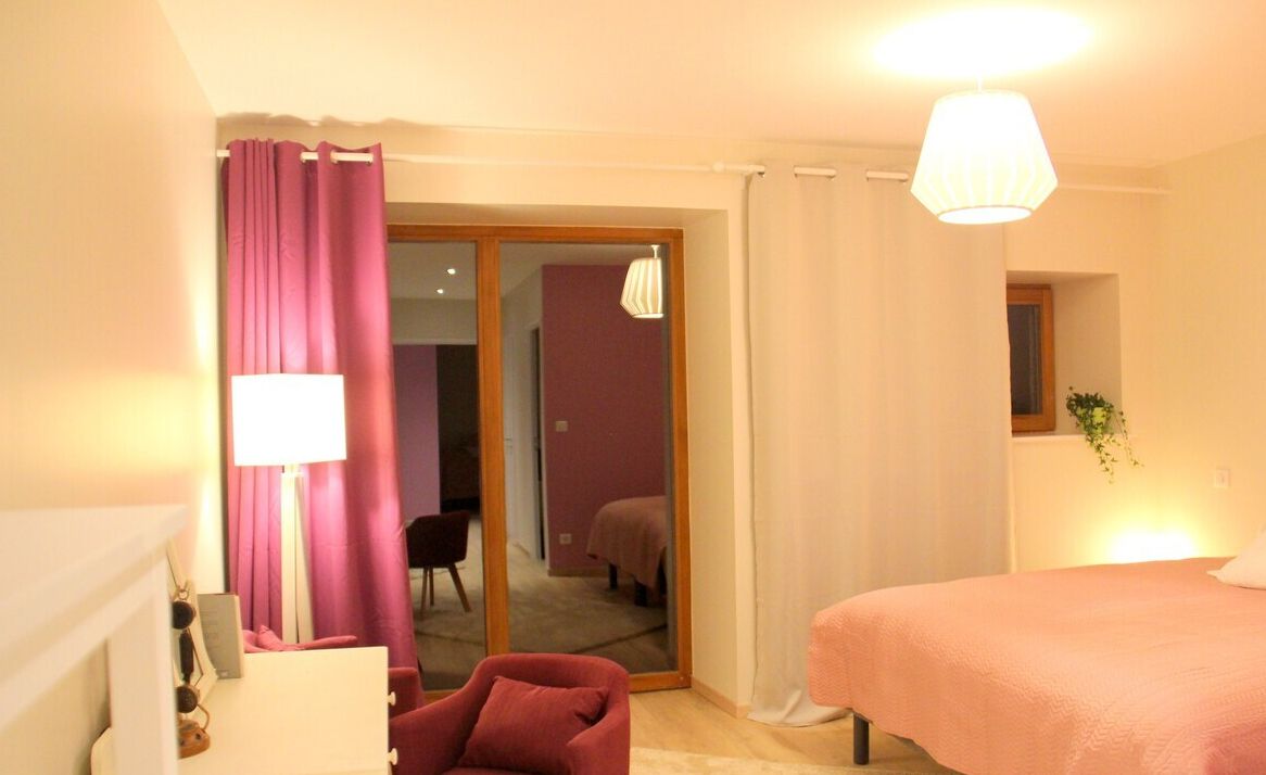 A bedroom with a bed, a desk with a lamp, a chair, and a sliding door leading to a bathroom.