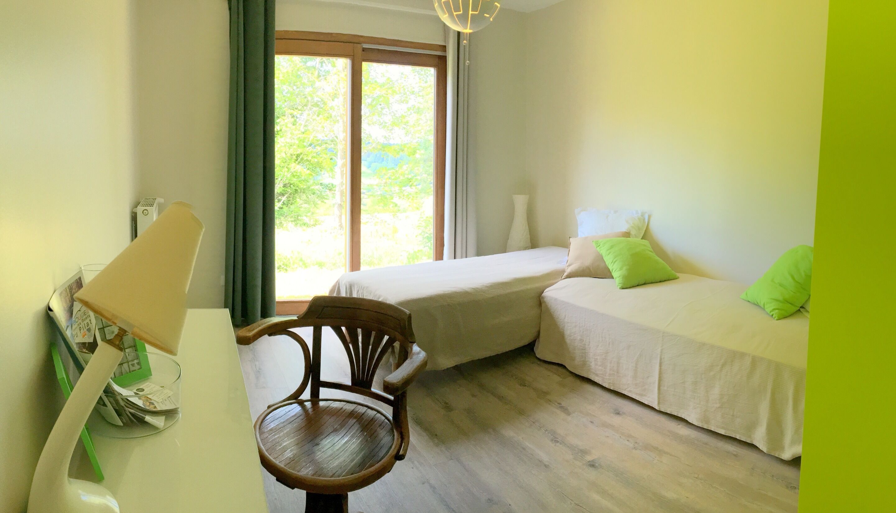 Una habitación con dos camas, una silla de madera, una mesa con lámpara y una ventana con cortinas.