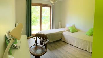 Una habitación con dos camas, una silla de madera, una mesa con lámpara y una ventana con cortinas.