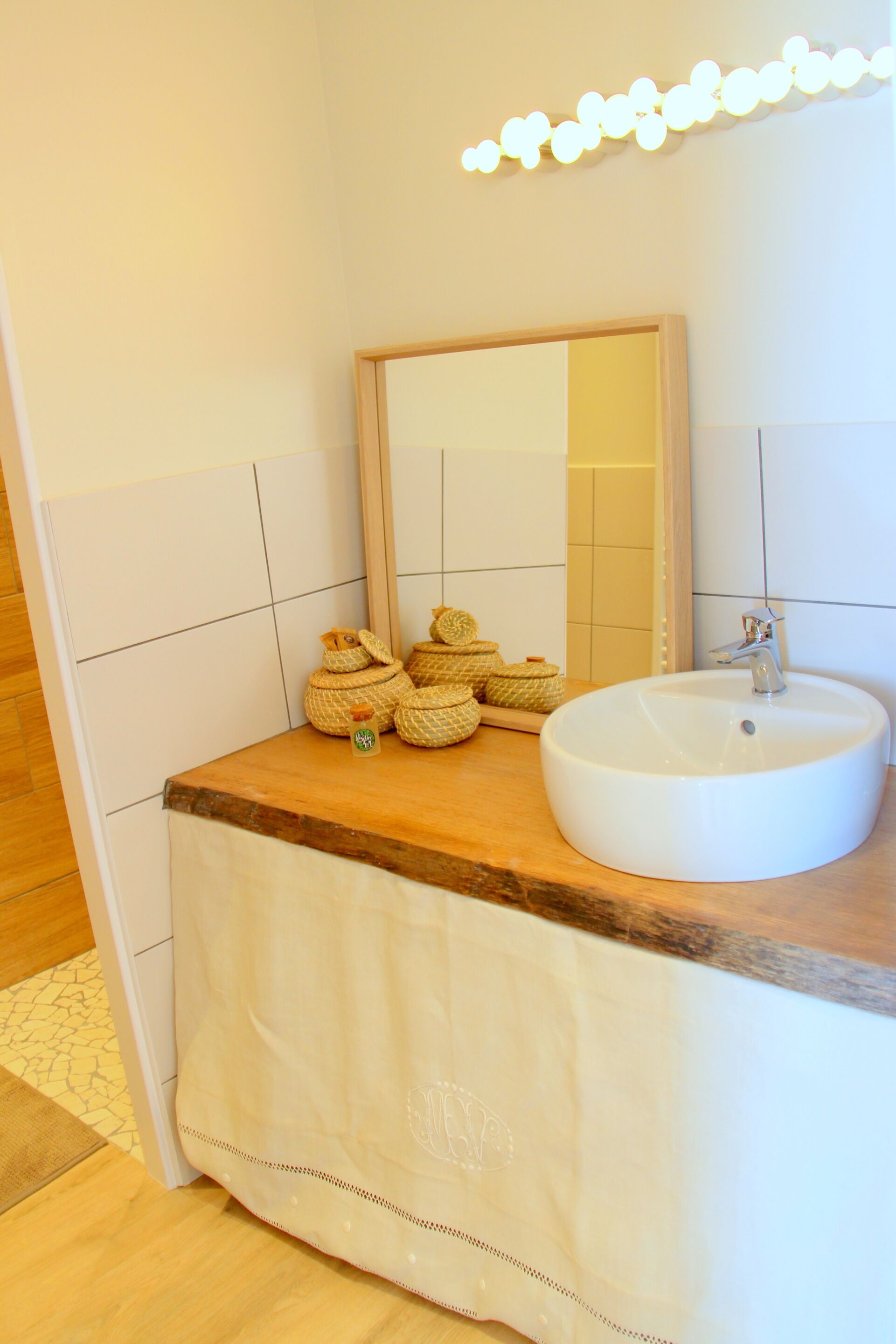 Un baño con encimera de madera, un lavabo blanco y un espejo encima. Hay cestas tejidas sobre la encimera.