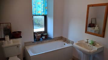Een badkamer met een bad, wastafel, toilet, raam met gordijnen en een spiegel.