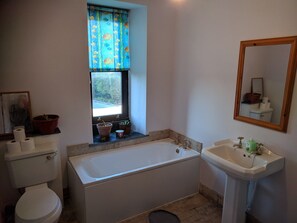 Une salle de bain avec une baignoire, un lavabo, des toilettes, une fenêtre avec des rideaux et un miroir.