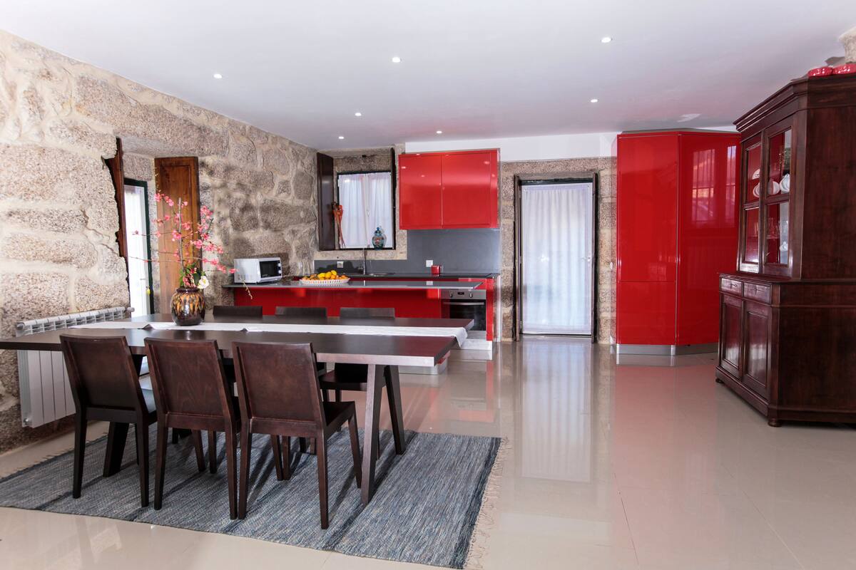 A modern kitchen with red cabinets, a dining area with a table and chairs, and a stone wall.