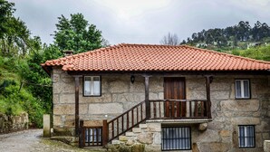 A stone building with a tiled roof, a wooden staircase, and barred windows. - Casa de Carcavelos (Cabeceiras de Basto)