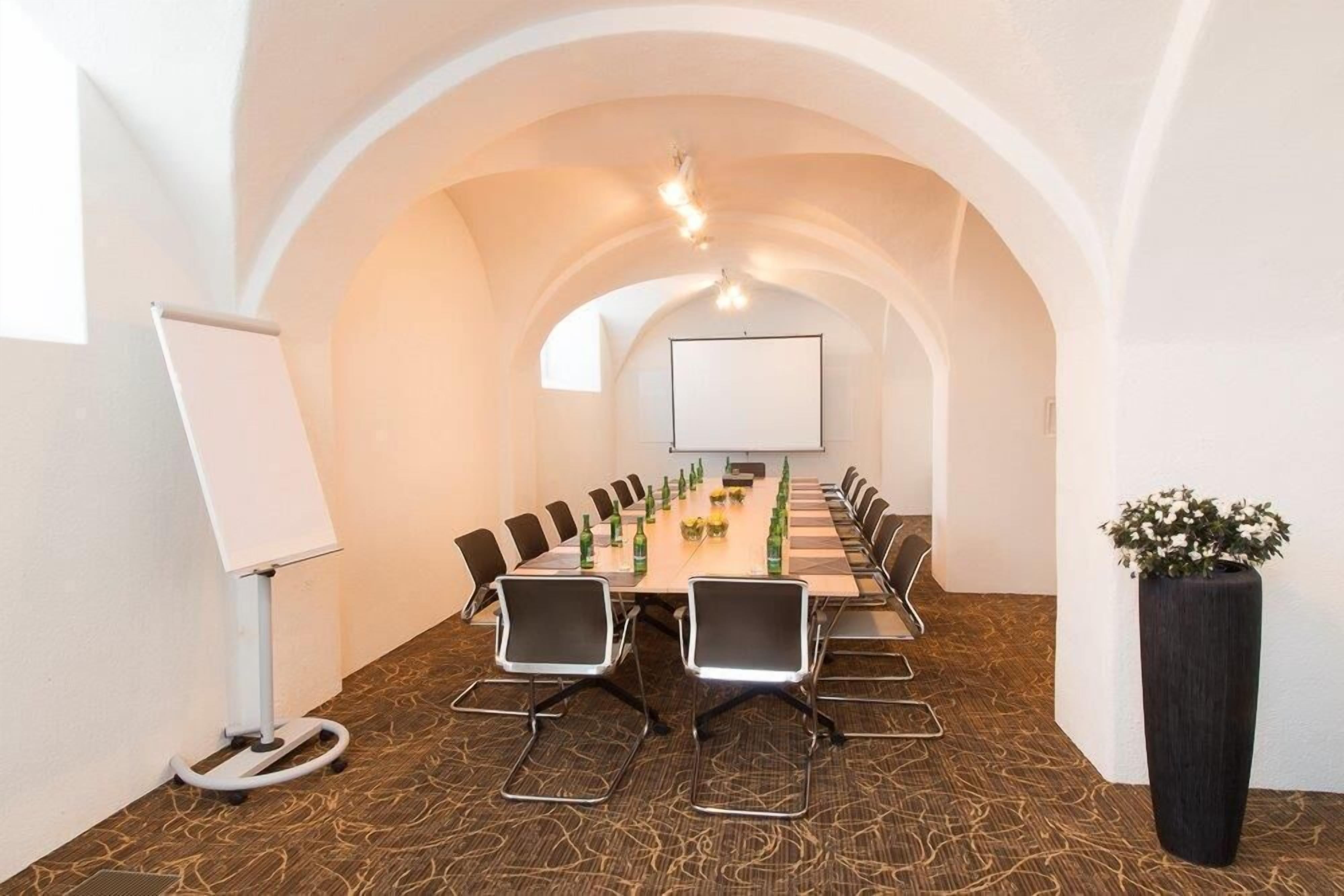 Ein Konferenzraum mit einem langen Tisch, Stühlen, einer Whiteboard-Tafel und einer Projektionsleinwand.